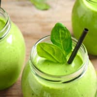 Jars of healthy green smoothie with fresh spinach on wooden table, closeup view